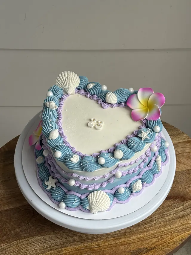 Blue, white and lavender heart cake with seashells, a plumeria flower and a 23