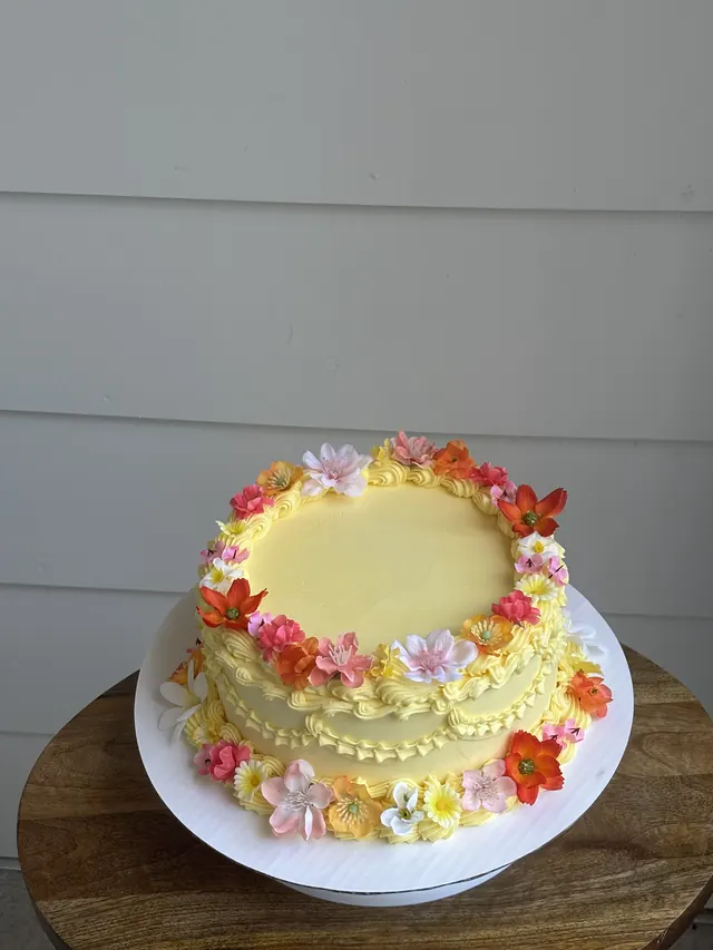 Pale yellow round cake ringed with bright orange, pink and yellow flowers