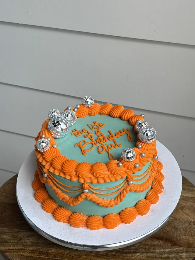 Teal round cake with orange piping, mini disco balls and an orange birthday message