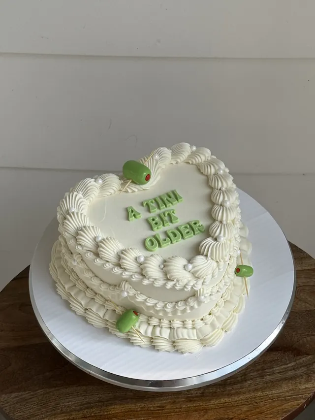 Ivory heart cake with green olives and "A TINI BIT OLDER" in green letters