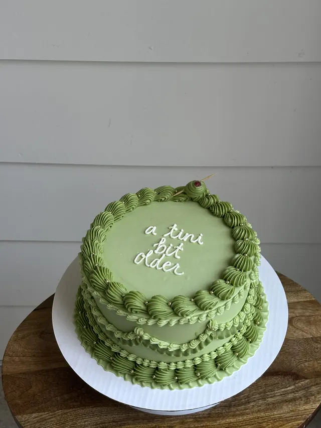 Olive green round cake with a piped olive and "a tini bit older."