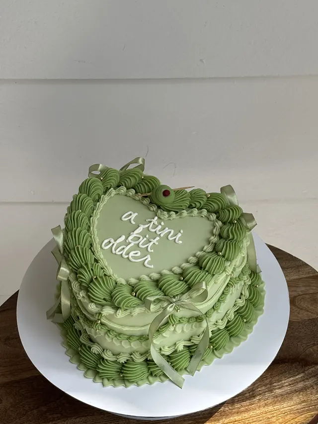 Sage green heart cake with green bows and "a tini bit older."