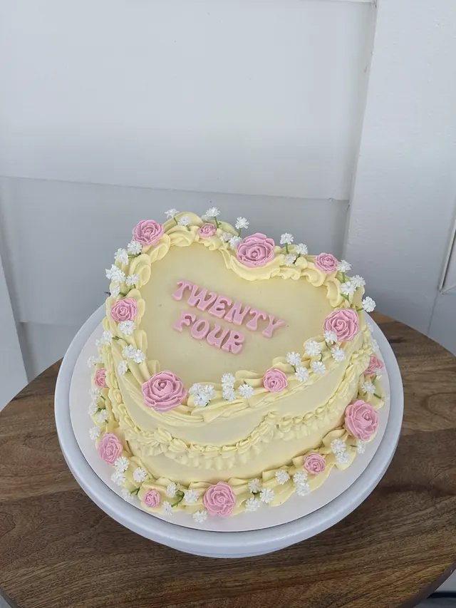 Pale yellow heart cake with pink roses and "TWENTY FOUR."