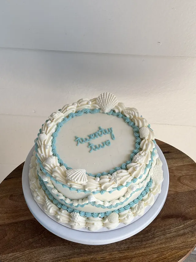 White round cake with blue piping, seashells and "twenty two."