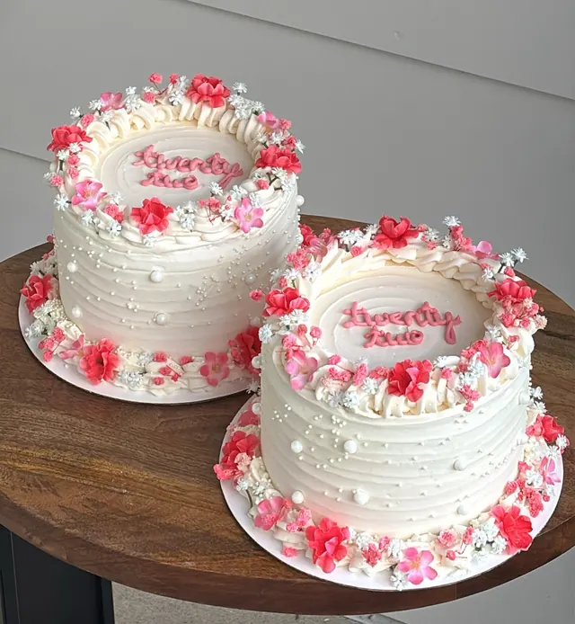 Two small white round cakes with pink and red flowers and pearls