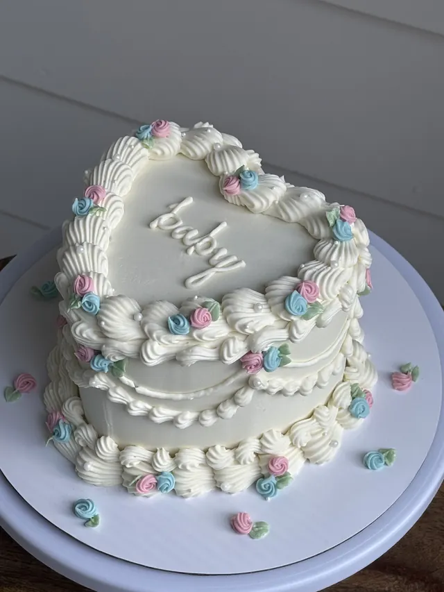 White heart cake with pink and blue rosettes and "baby."