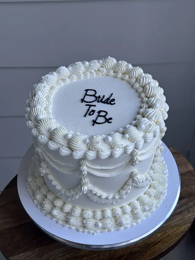 White round cake with swag piping, pearls and "Bride To Be."