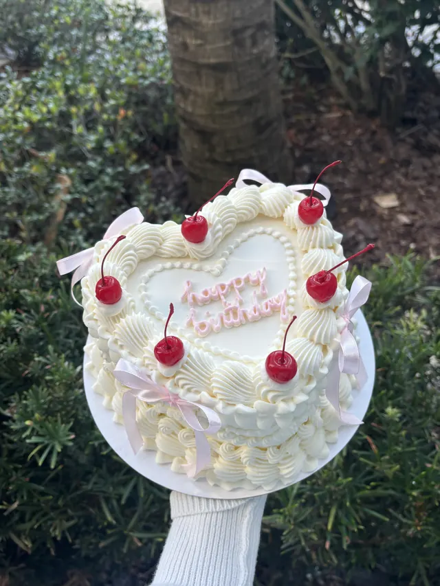 White heart cake with cherries, pink bows and "happy birthday" in pink