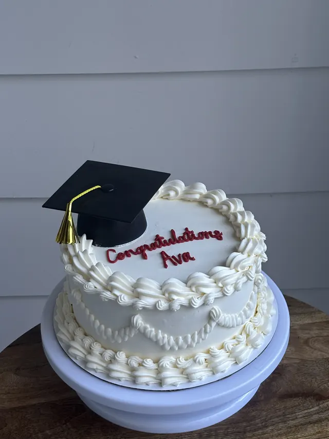 White round cake with a graduation cap topper and a red congratulations message